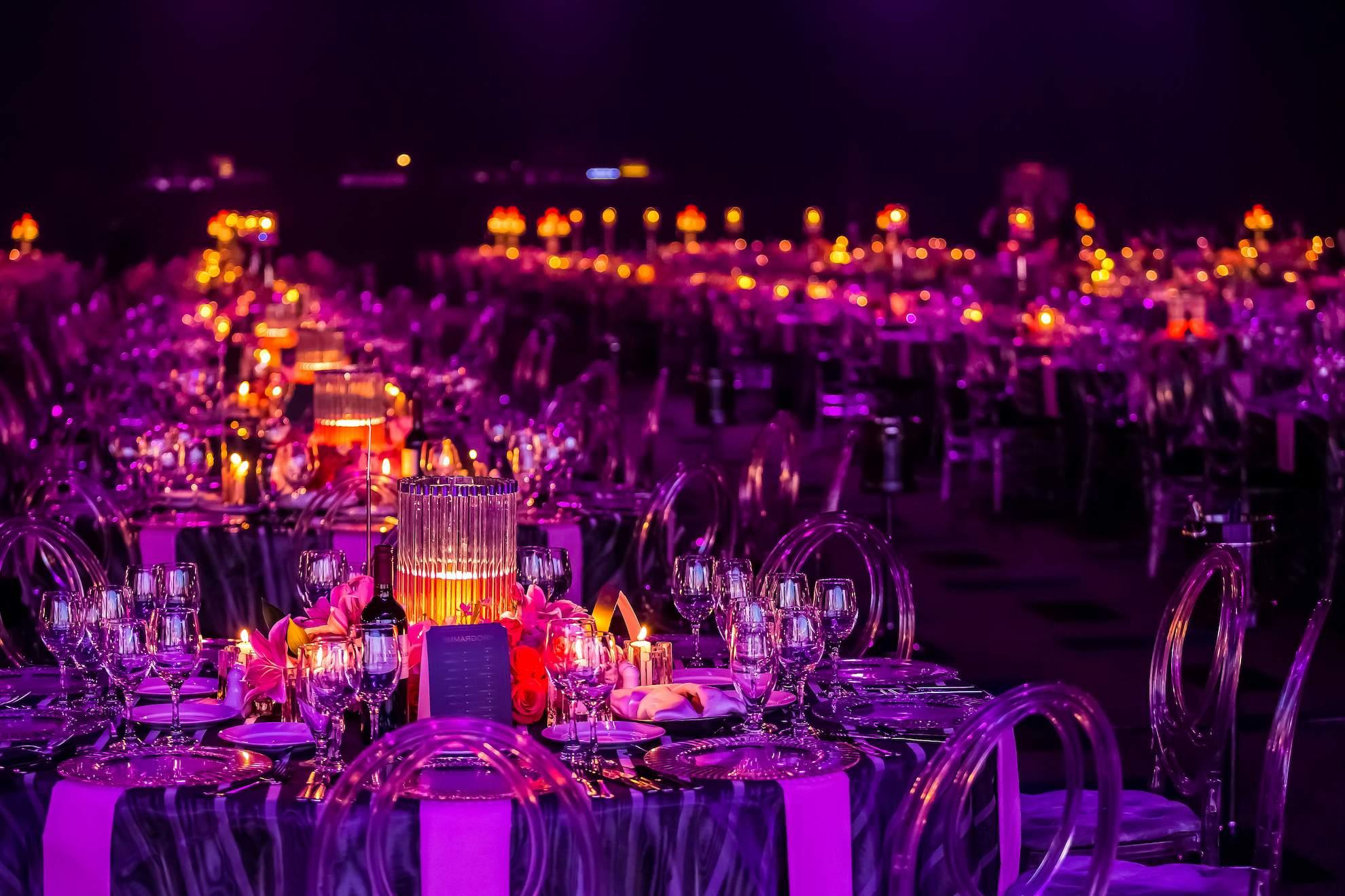 Elegant charity gala dinner tables with purple event lighting.
