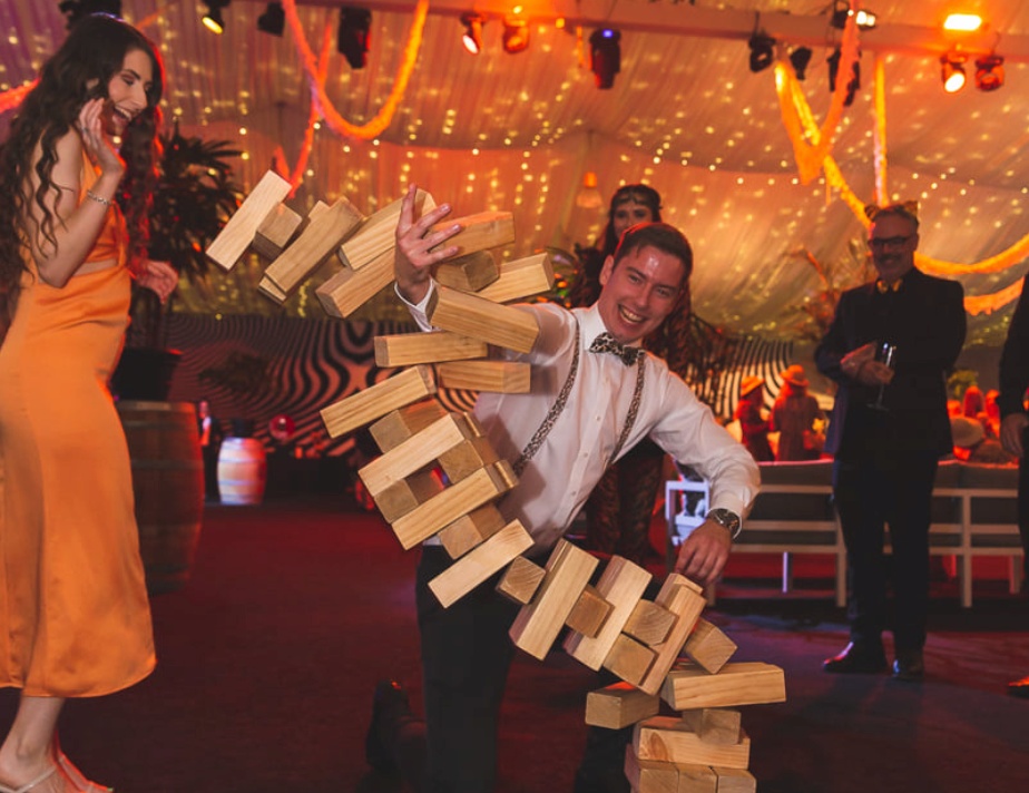 Wedding guests laughing while playing giant Jenga during a reception.
