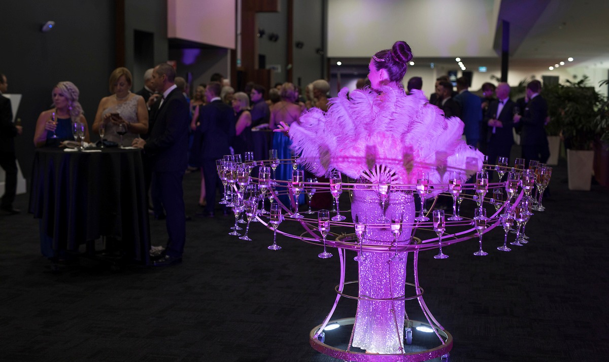 Champagne skirt performer serving drinks to guests during cocktail hour at a wedding reception.