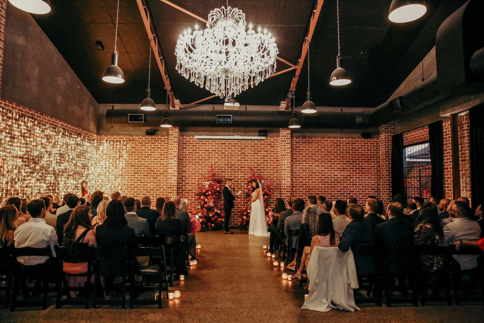 Wedding ceremony at Factory51 Brisbane with exposed brick walls, chandelier lighting and floral ceremony styling.