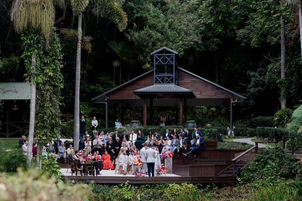 Rainforest wedding ceremony at Rainforest Gardens near Brisbane with guests seated around a timber amphitheatre and lush tropical greenery.