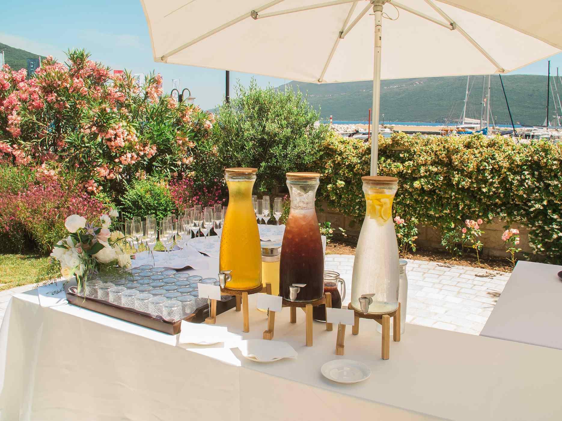 Outdoor summer drinks station with juices and glasses under a large umbrella.
