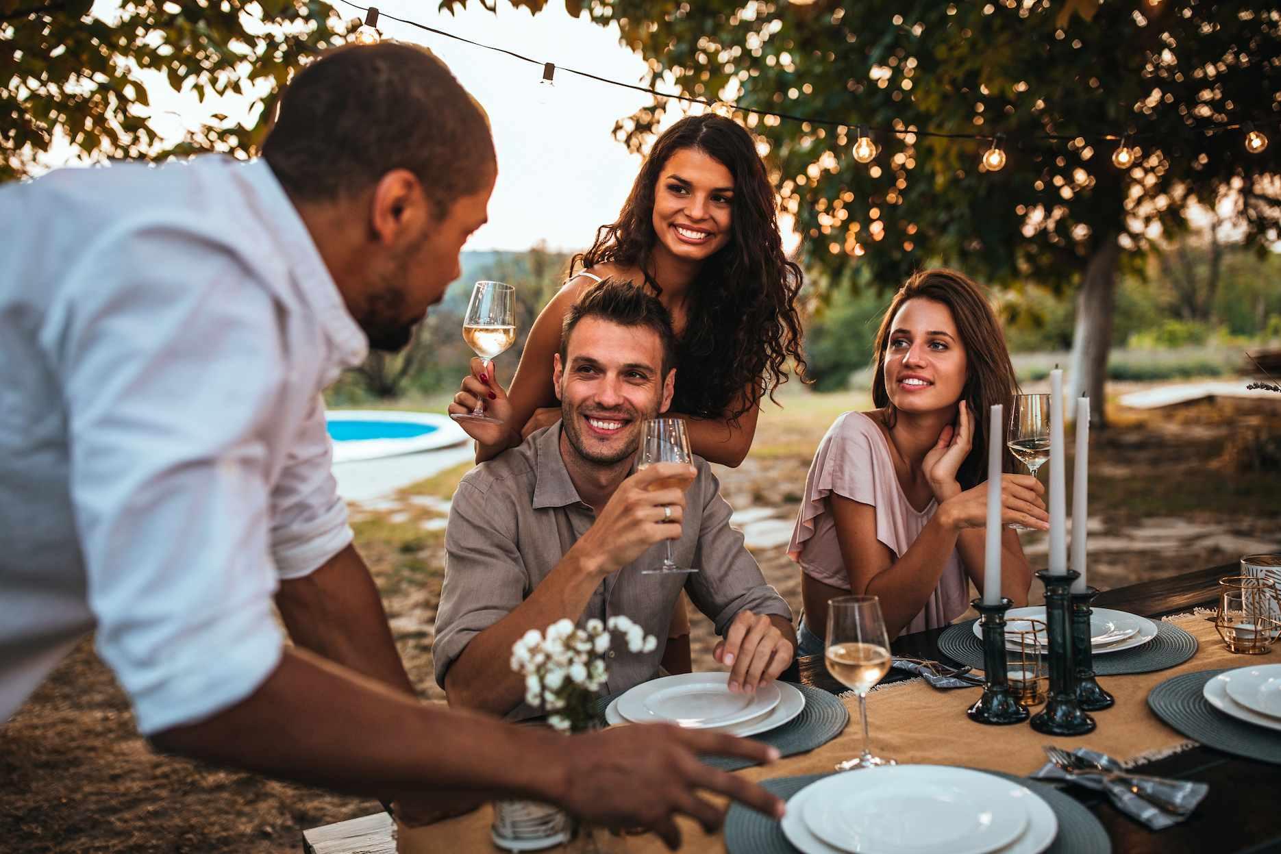 Friends enjoying a summer dinner party outdoors with drinks and festoon lighting.