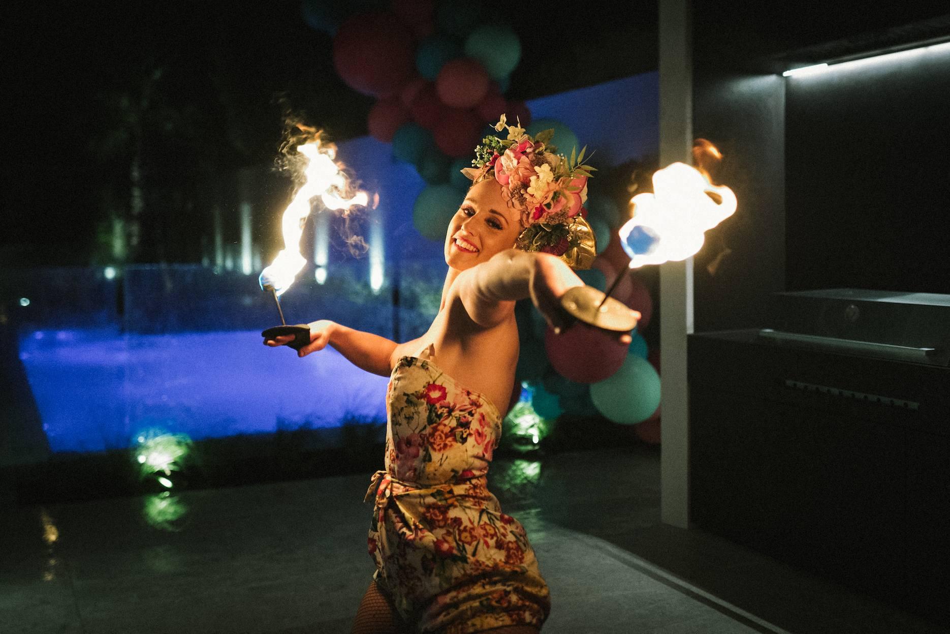 Fire performer entertaining guests at a poolside summer party at night.