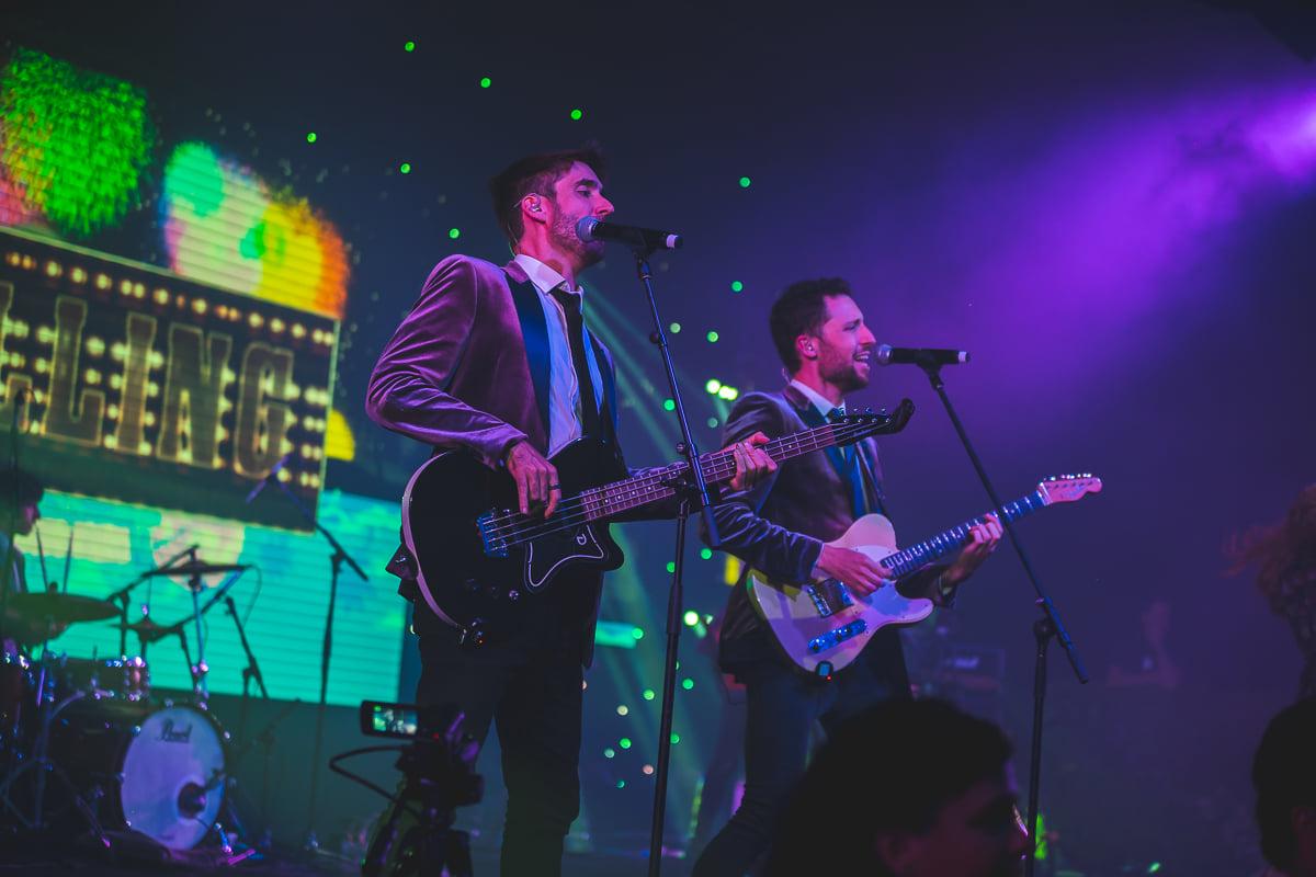 Live wedding band performing on stage, with a bassist and guitarist singing under vibrant purple and green lighting.
