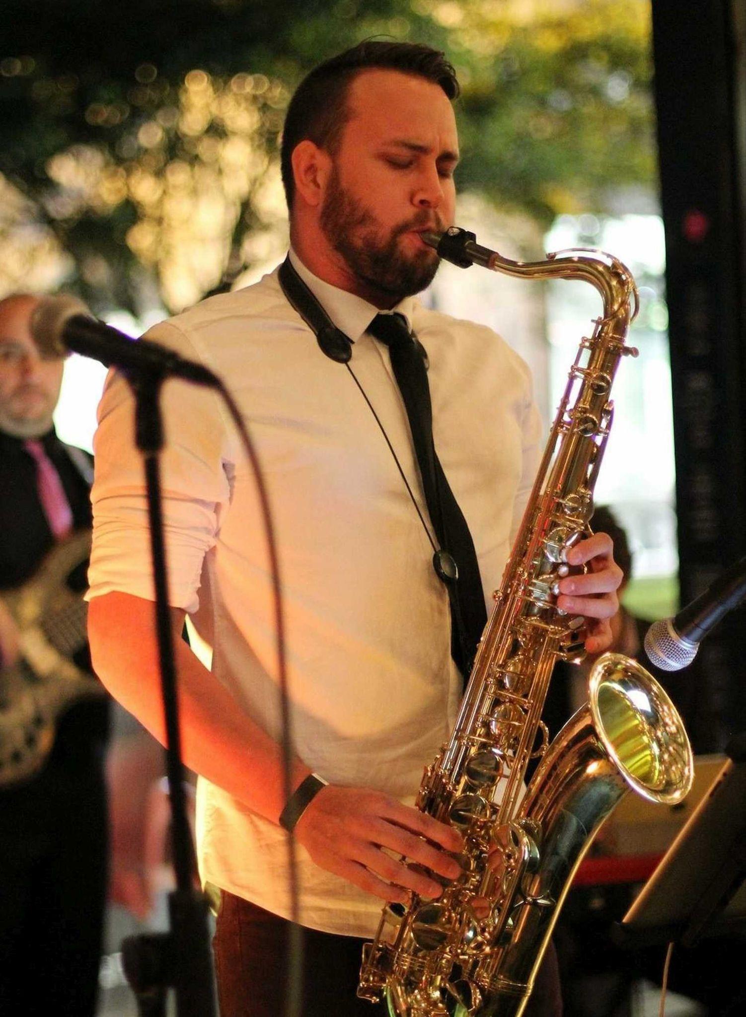 Saxophonist performing live beside microphones and band equipment at an event.