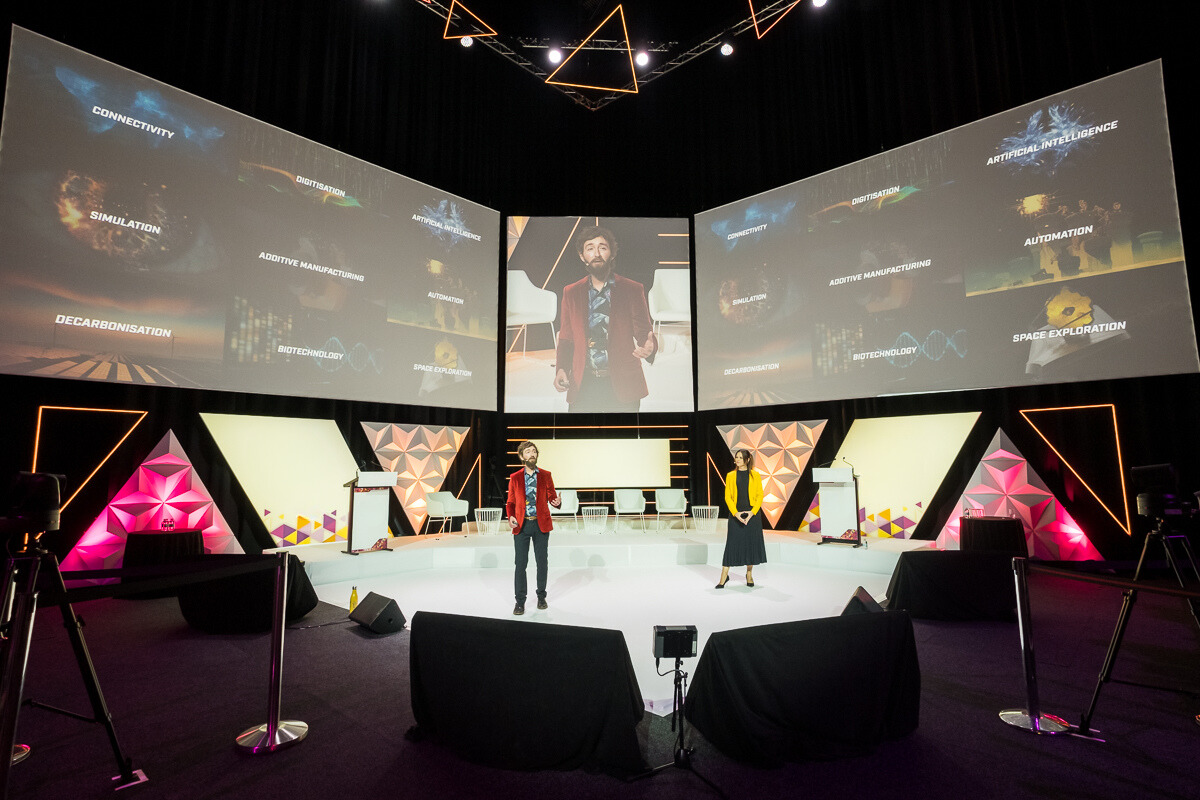 Keynote speaker presenting on AI and emerging technology at a corporate conference with large stage screens.