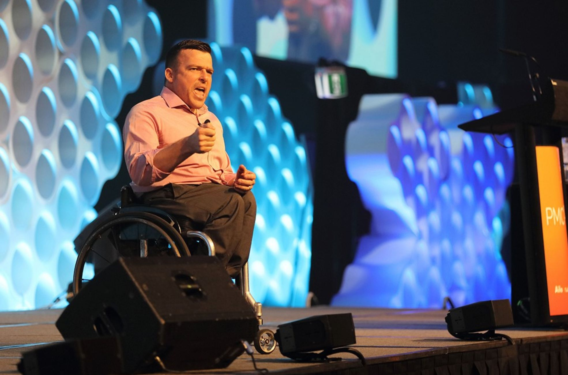 Male keynote speaker in a wheelchair presenting on stage at a corporate conference in Australia.