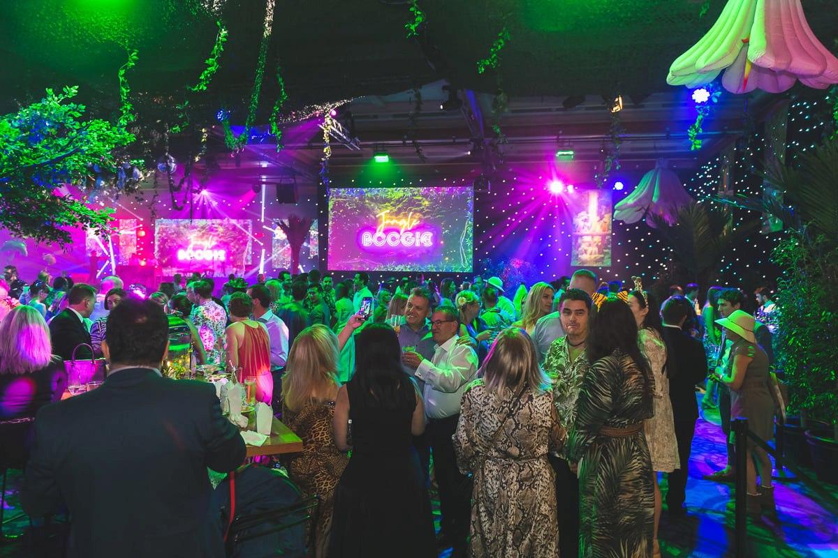 Guests networking at a professionally produced corporate event with colourful lighting and stage entertainment.
