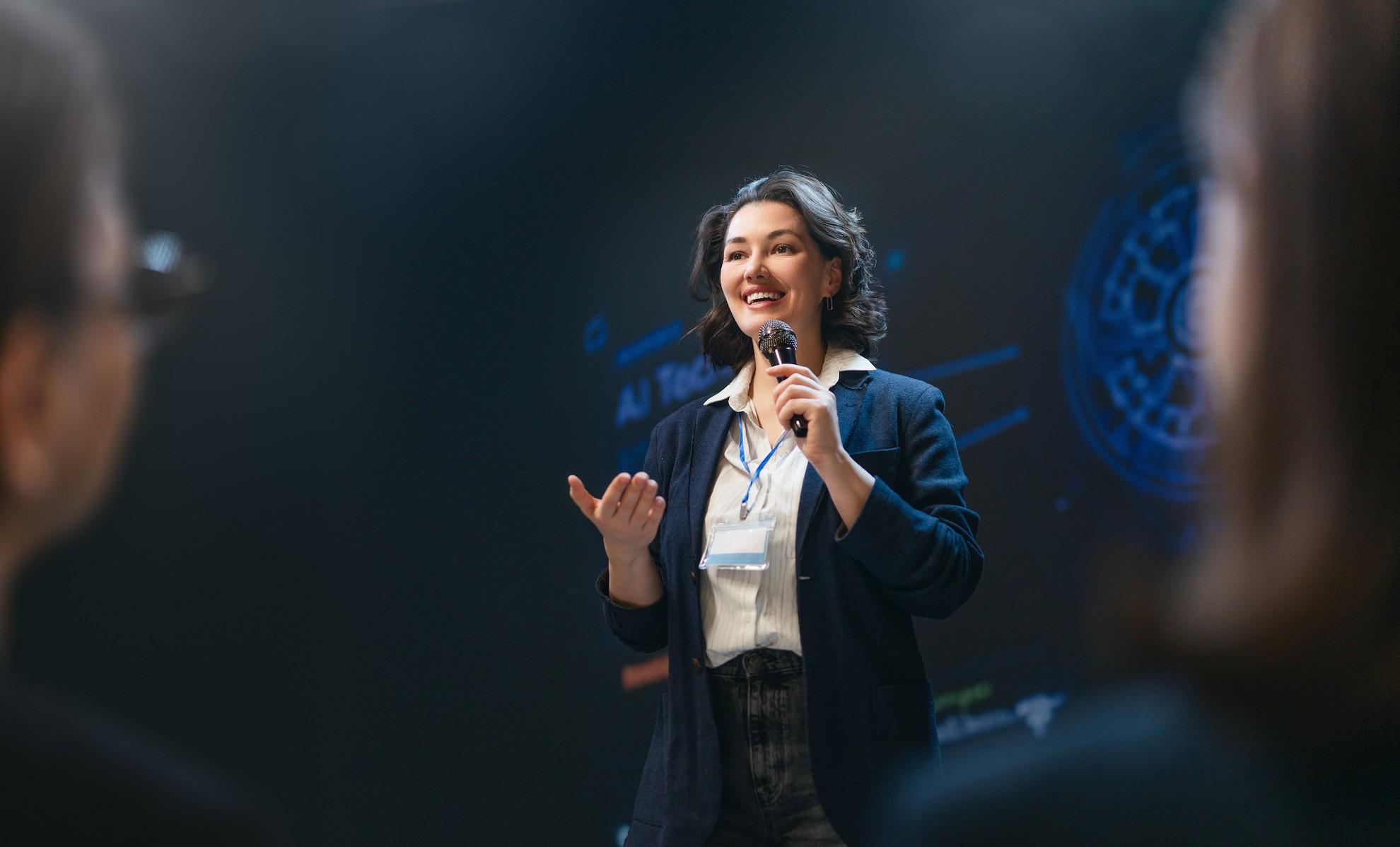 Professional event MC speaking into a microphone while engaging guests at a corporate product launch.