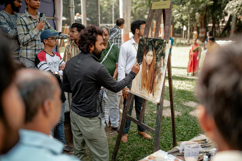 Indian man doing a live painting at an event surrounded by attendees