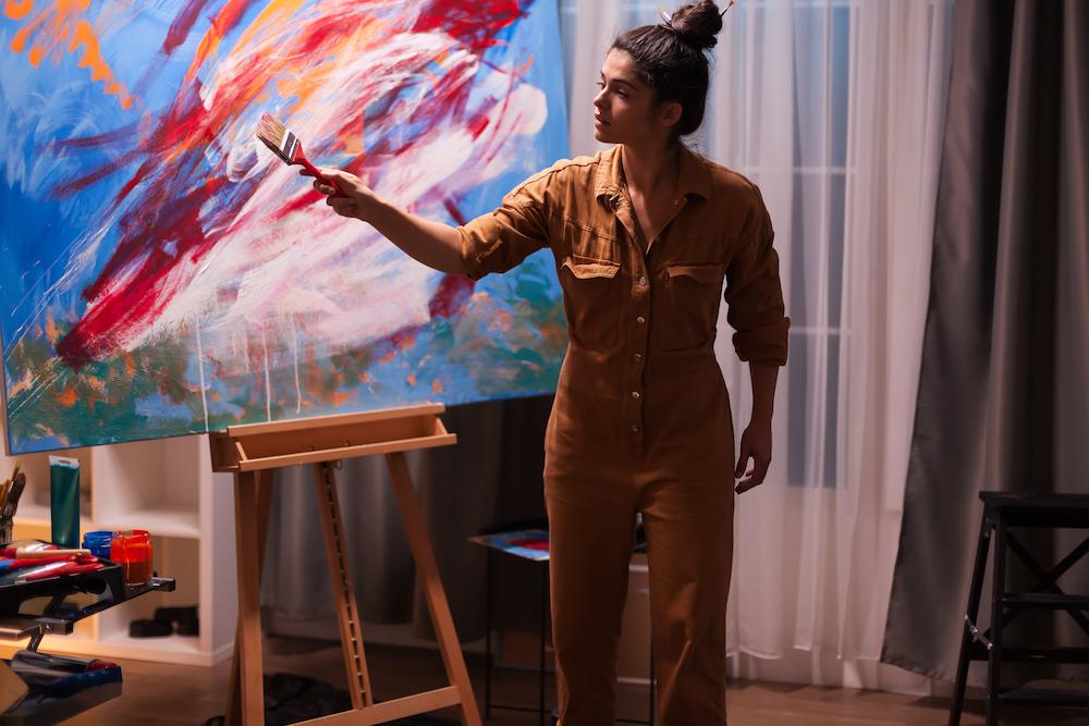 Live painting by a young female artist in an abstract style with reds and blues on a large canvas