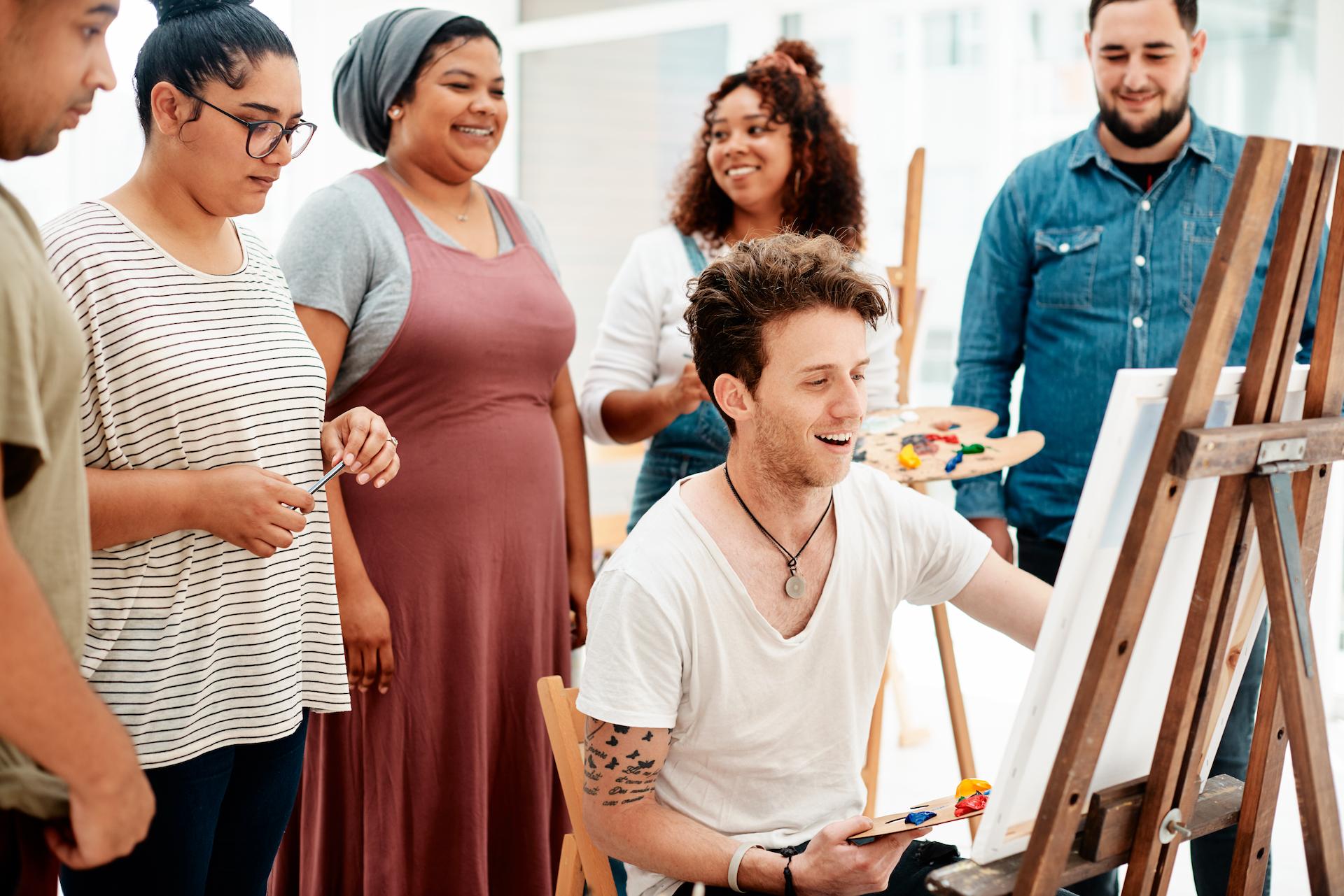 Live painting demonstration at an event with people crowded around the canvas, watching the artist work