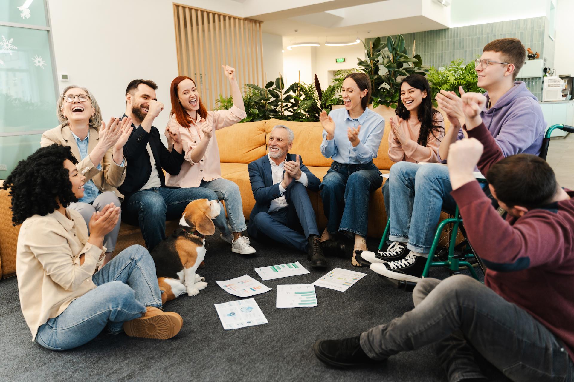 Group of employees in an office engaging in audience participation games for morale boosting all cheering and laughing