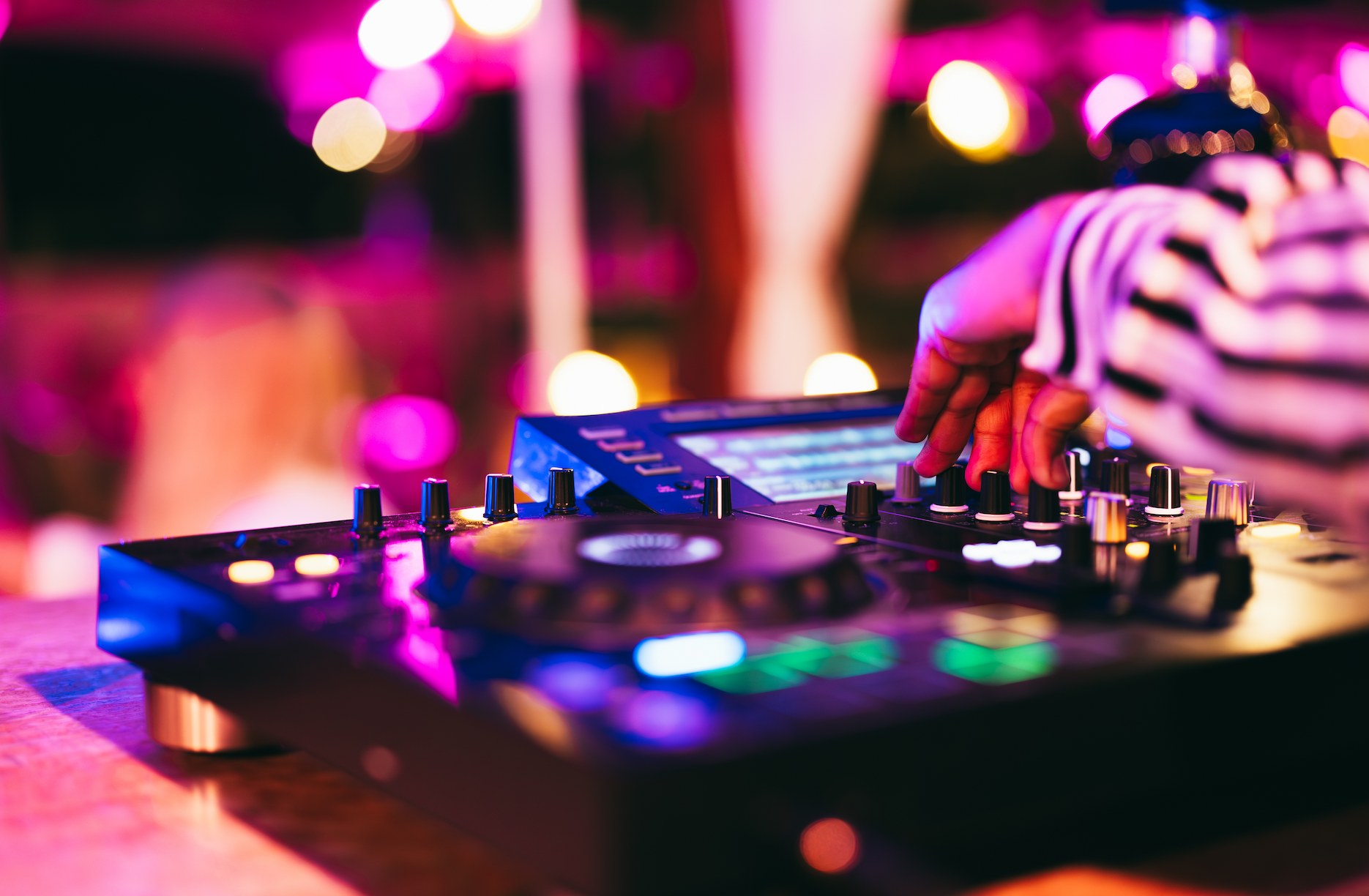 Professional wedding DJ adjusting music on a controller during a reception with colourful lighting.