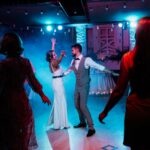 Bride and groom sharing their first dance at a wedding reception with atmospheric lighting and a lively dance floor.