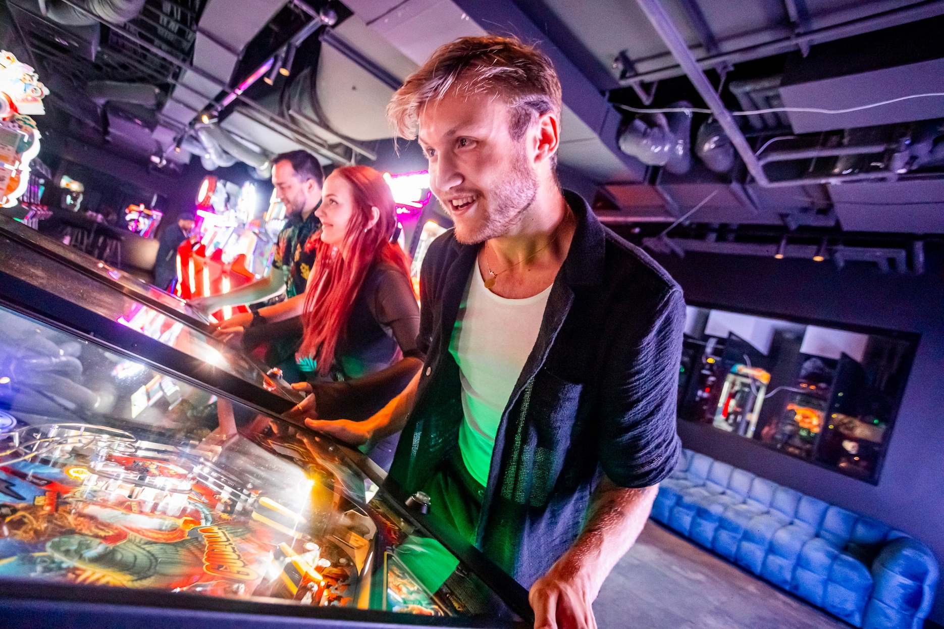 Guests playing arcade and pinball games together at a party.