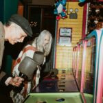 Adults playing a whack-a-mole arcade game at a retro-themed party.