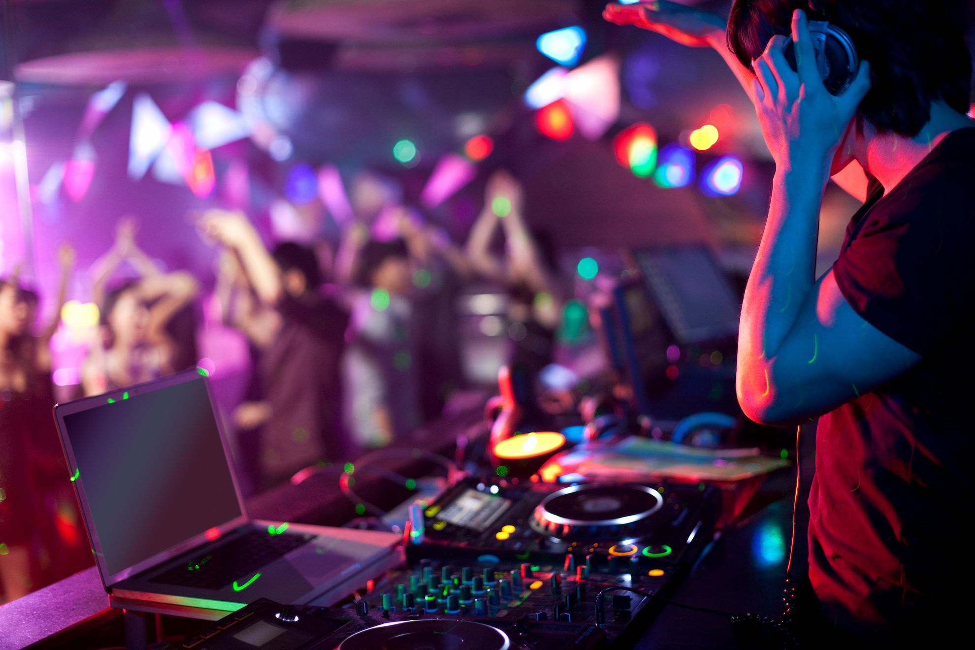 A DJ performing at a neon-coloured retro arcade party, with people dancing in the background.