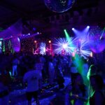 Neon-lit dance floor and disco ball at a lively 80s themed party.