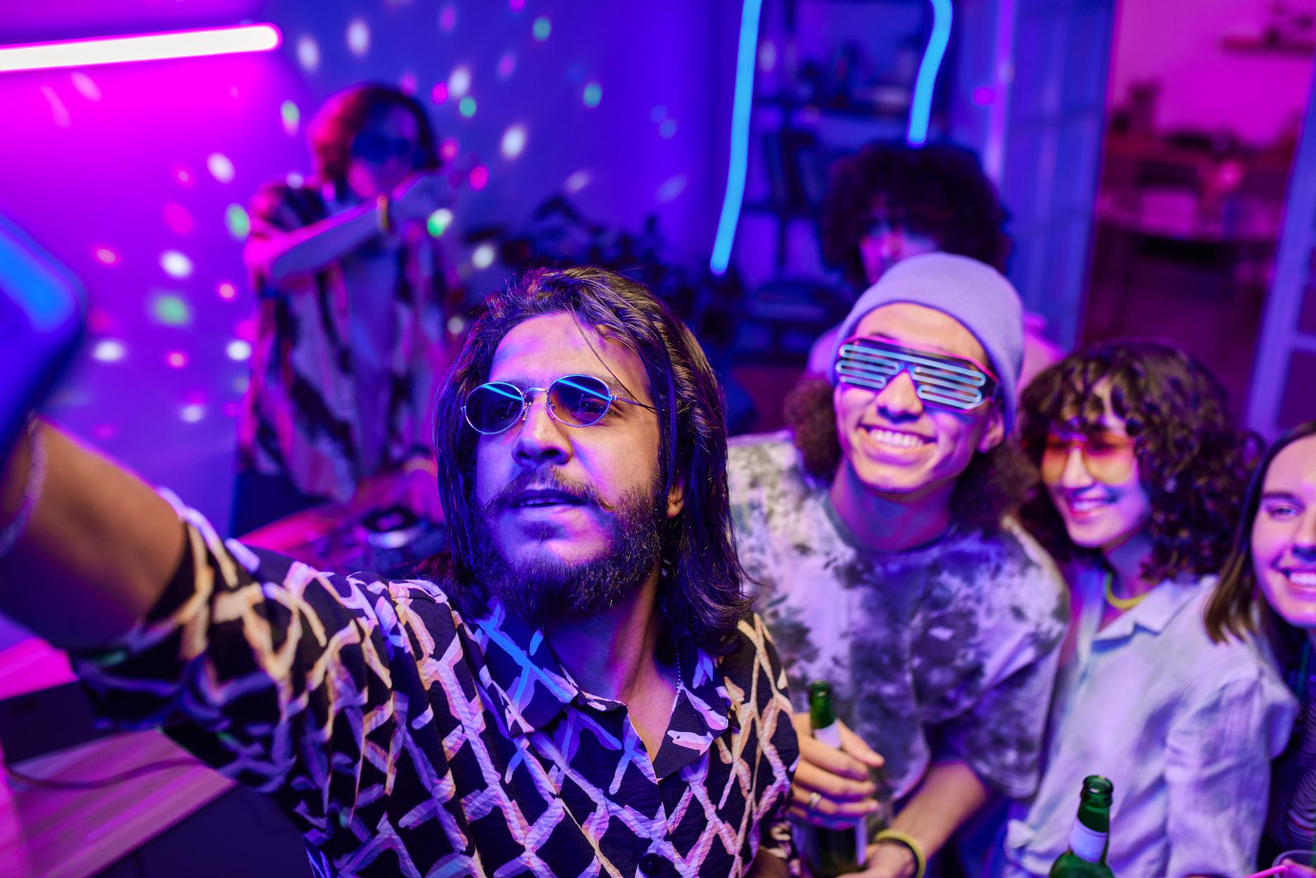 Guests in retro sunglasses taking a selfie at a neon 80s party.