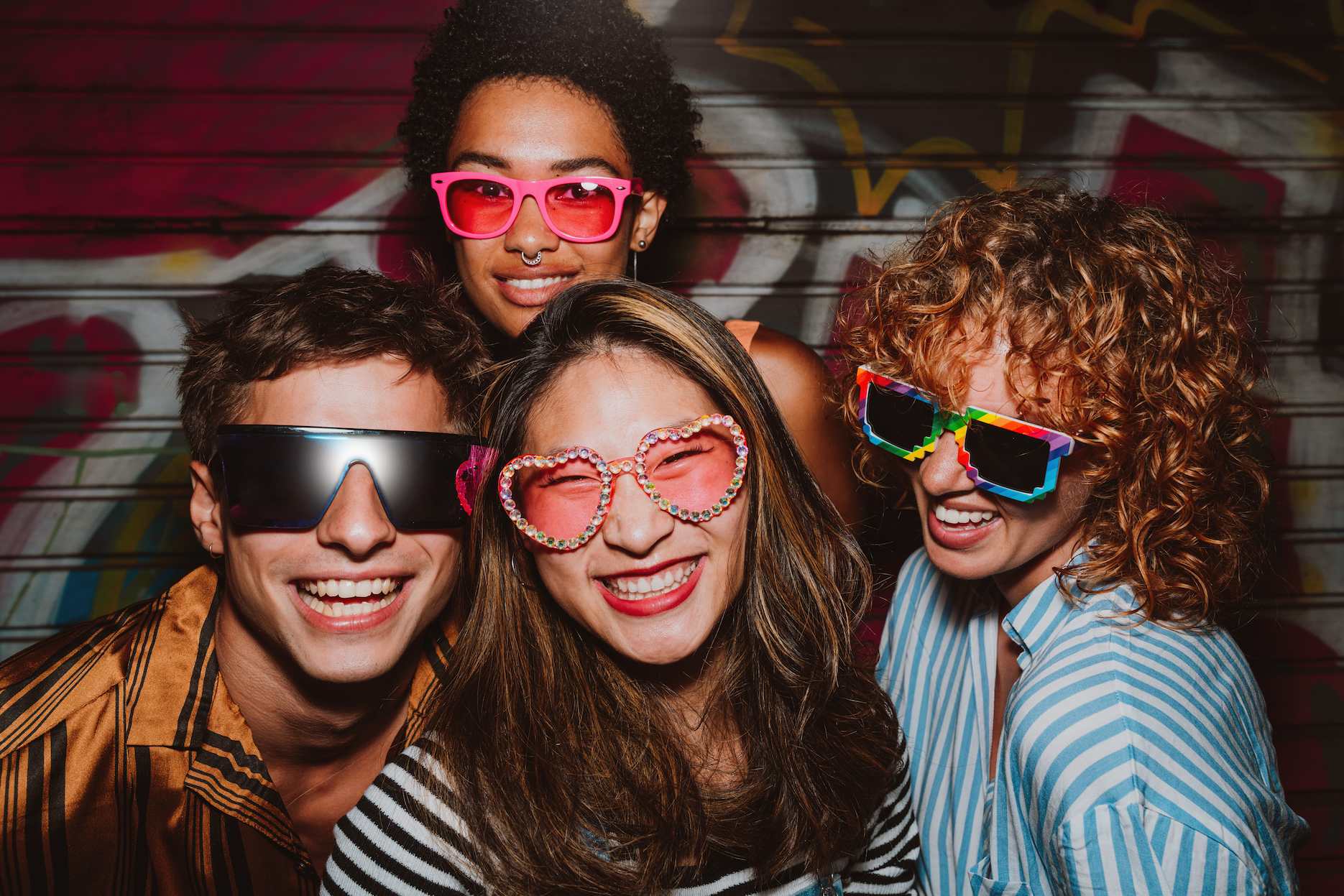 Group of friends posing in colourful retro glasses at an 80s themed party.