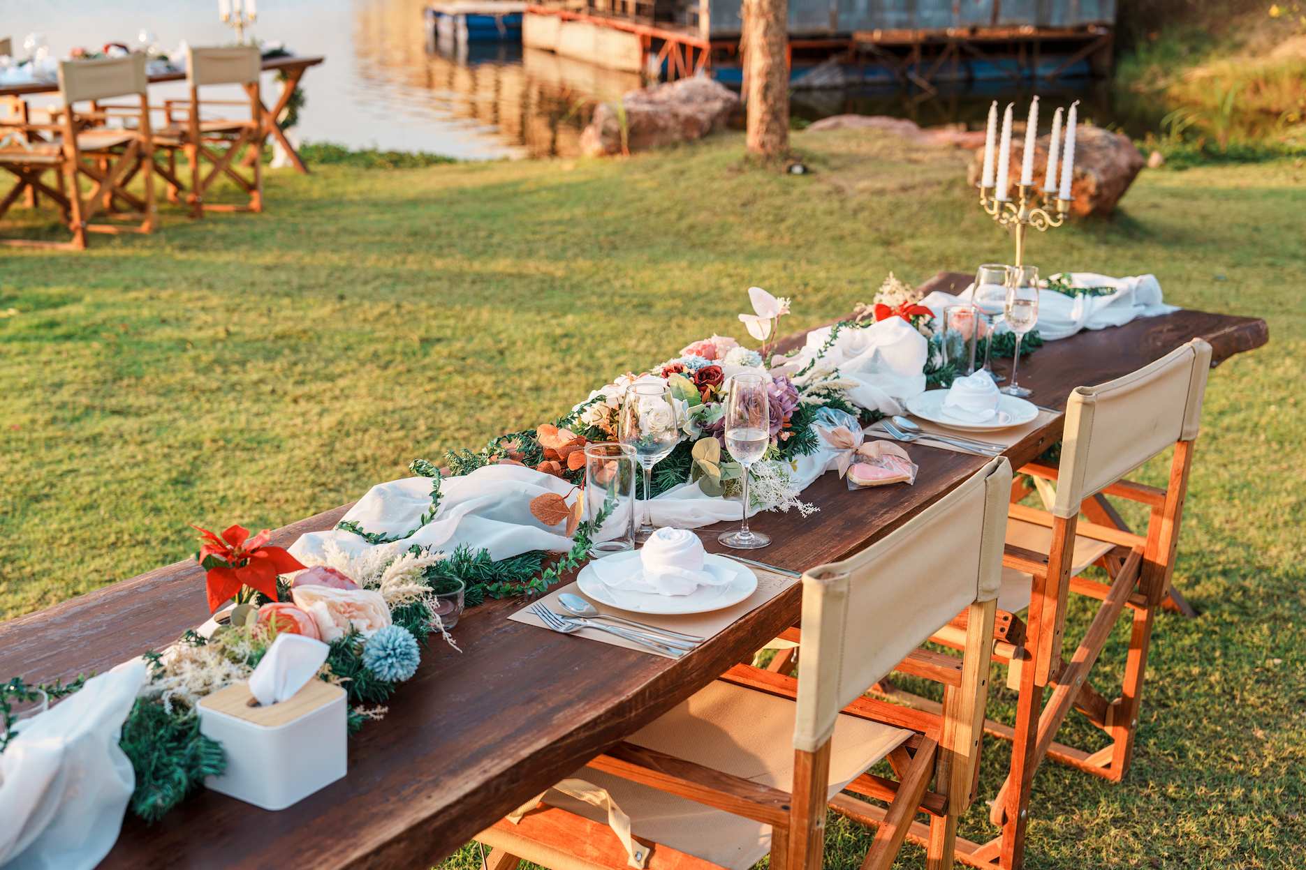 Elegant outdoor long-table setup by the water for engagement party ideas, with floral styling and sunset light.