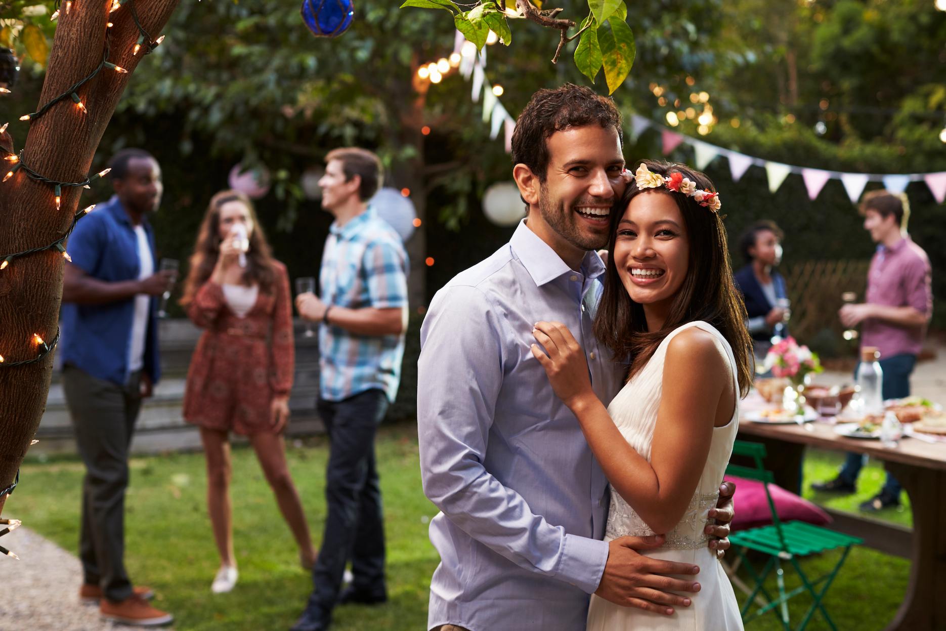 Engagement-party-ideas-4 Happy couple at a backyard engagement party with guests, festoon lights and relaxed garden celebration styling.