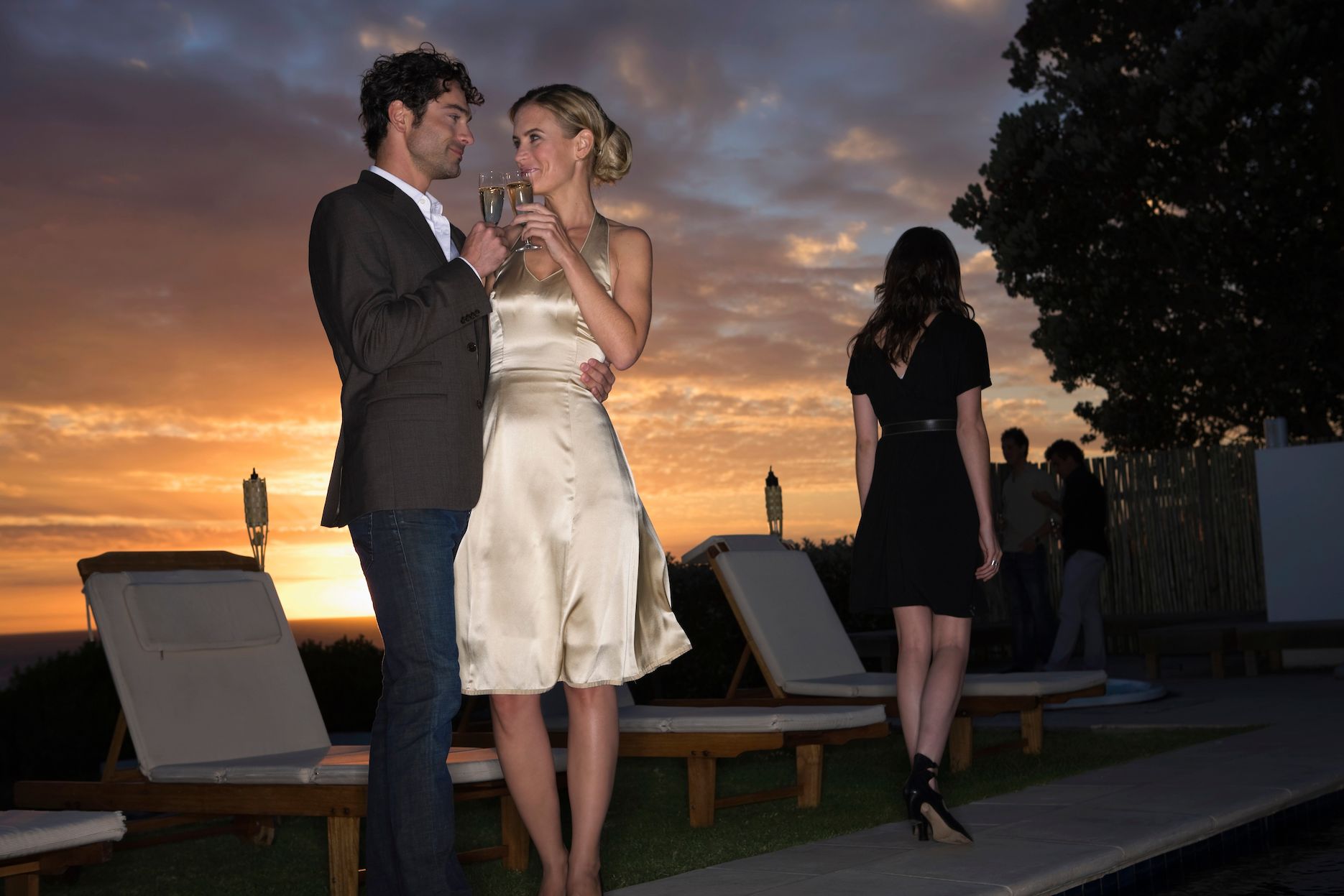 Couple toasting drinks at sunset during a rooftop engagement party with romantic evening atmosphere.