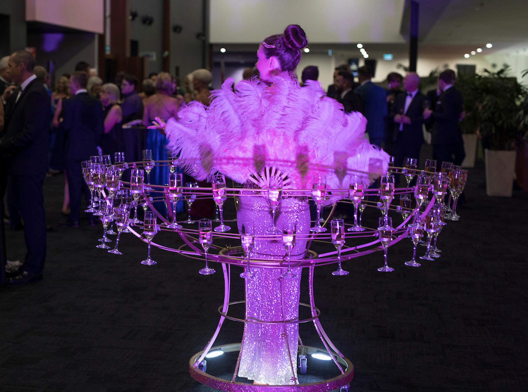 Champagne hostess in a feather costume providing roving entertainment at a gala reception.