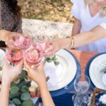 Guests toasting pink drinks at a styled outdoor bridal shower table with grazing food and florals.