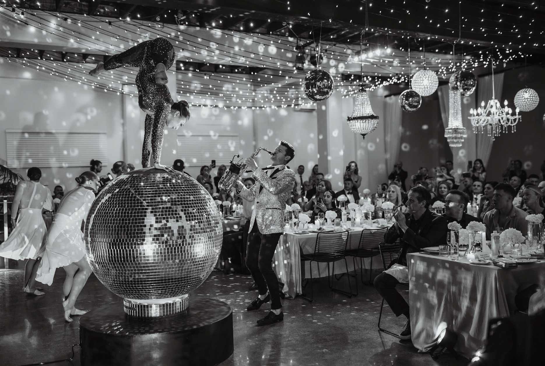 Giant disco ball performer with saxophonist at a glamorous disco party event.