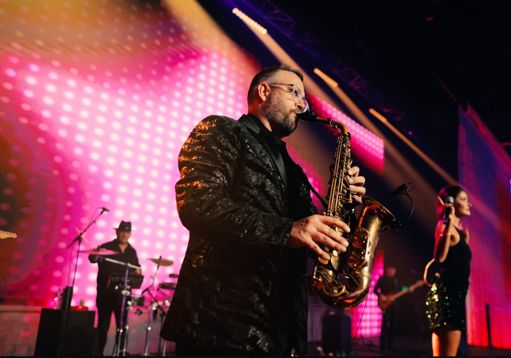Saxophonist performing with live band at a disco theme party.