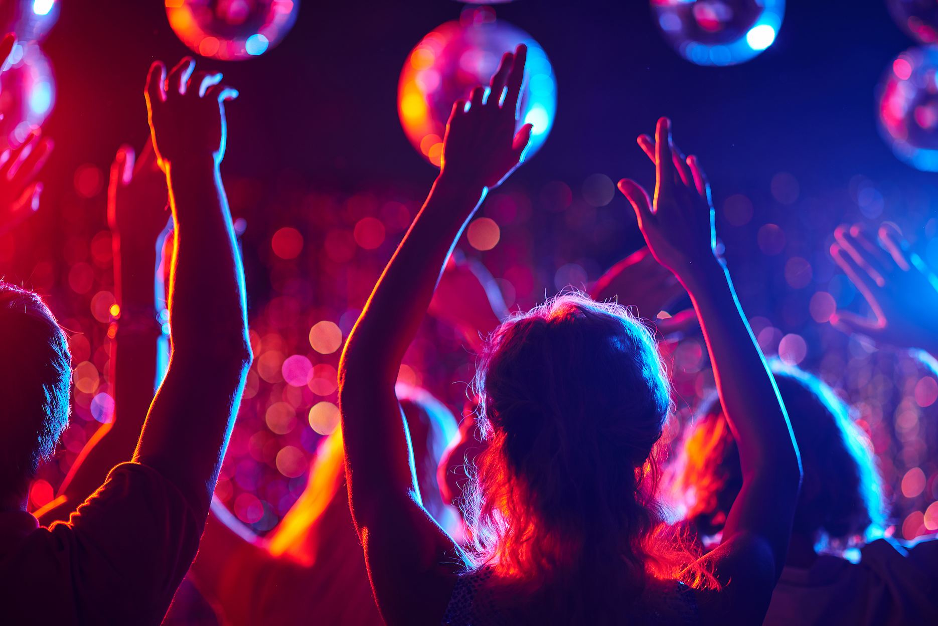 Guests dancing under disco balls and colourful lights at a disco theme party.
