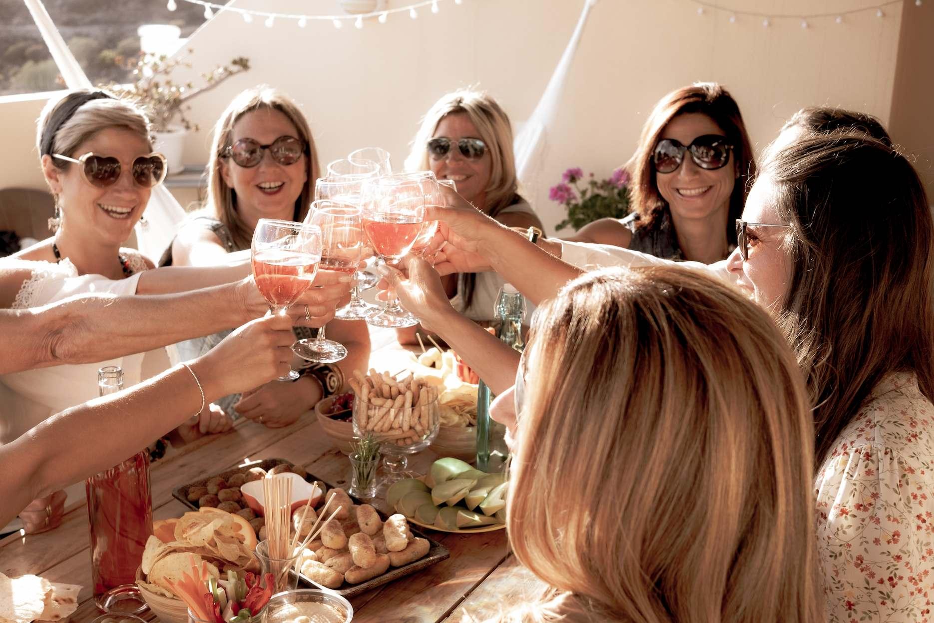 Women toasting rose at a relaxed bridal shower lunch with shared grazing plates.