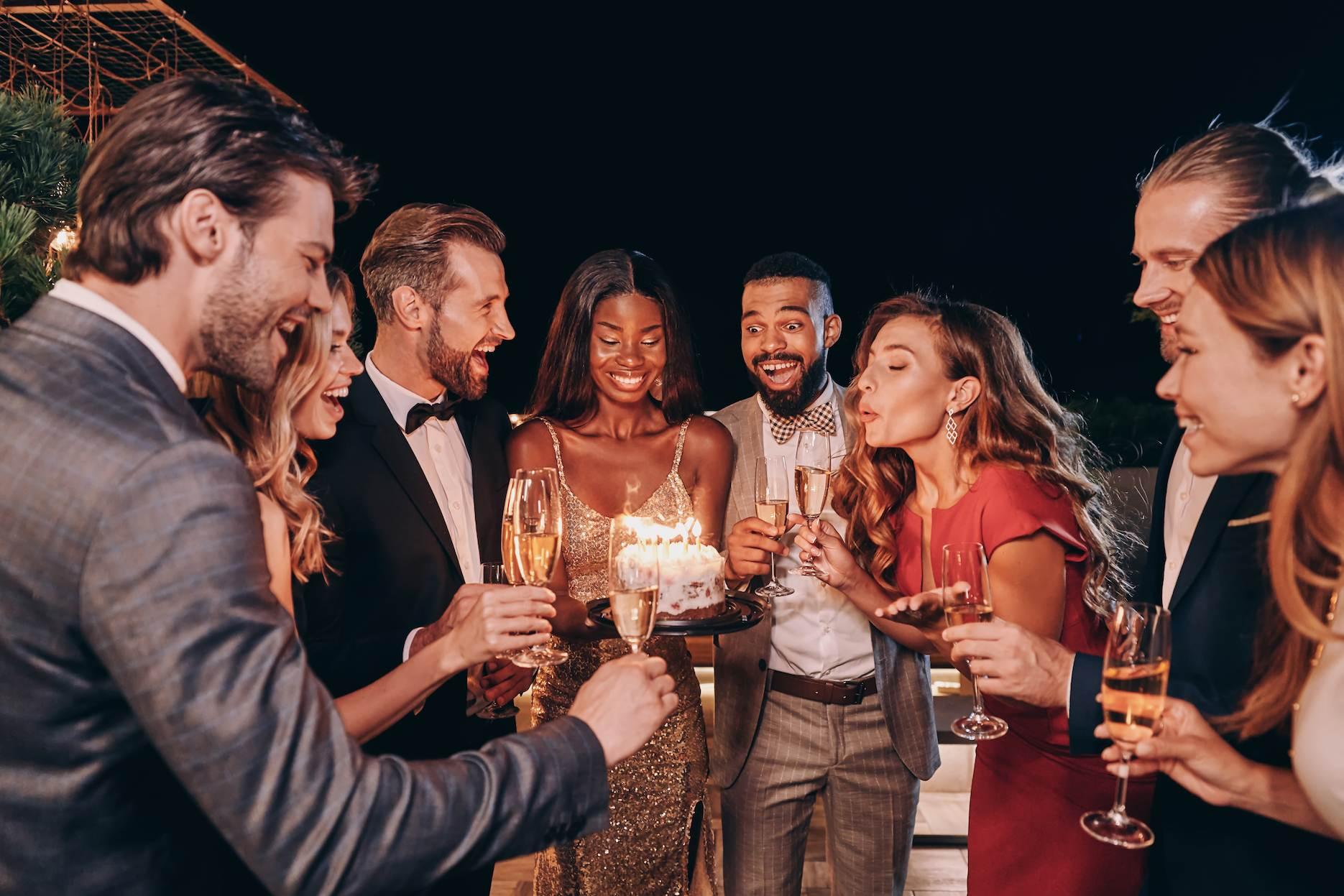 Friends celebrating an adult birthday party with cake and sparkling wine.