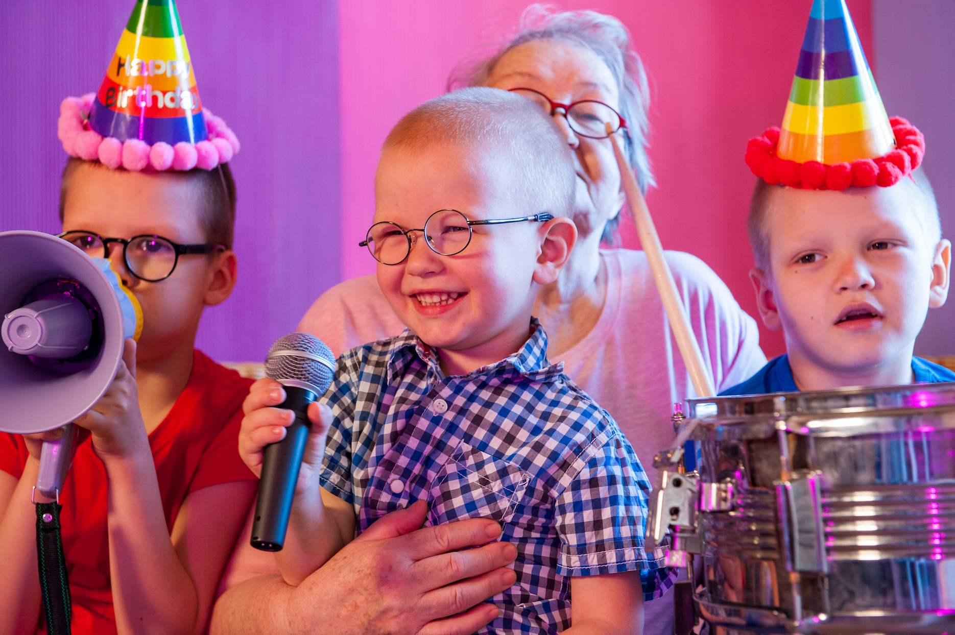 Children wearing birthday hats and singing with microphones at a colourful karaoke party.