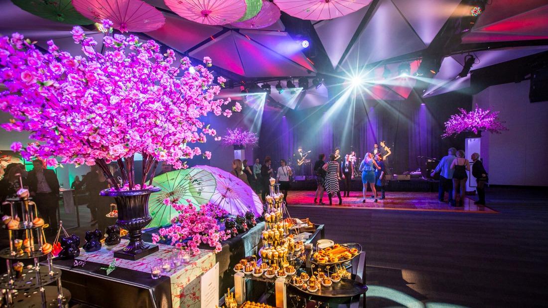 Corporate celebration with live music, guests dancing, pink floral displays and a dessert buffet.