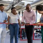 Business team smiling as they cut a red ribbon together inside a modern office during an official opening.