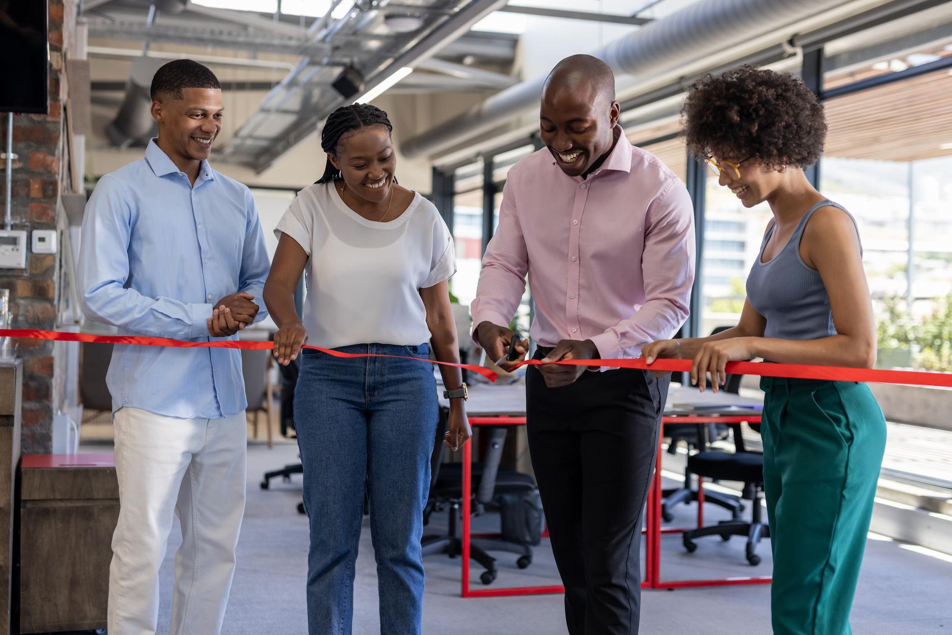 Business team smiling as they cut a red ribbon together inside a modern office during an official opening.