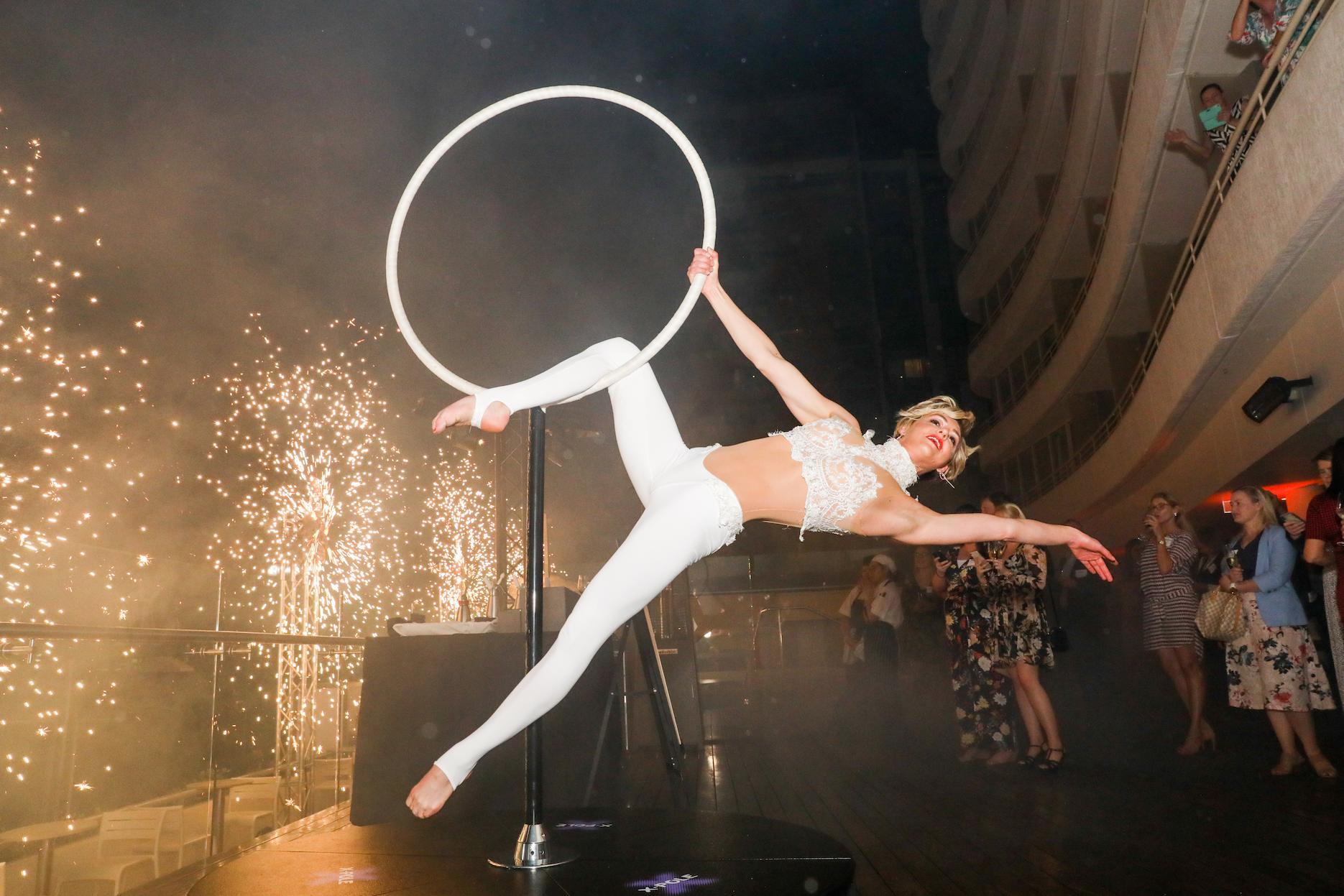 Aerial hoop performer presenting a feature act with theatrical spark effects at an event venue.