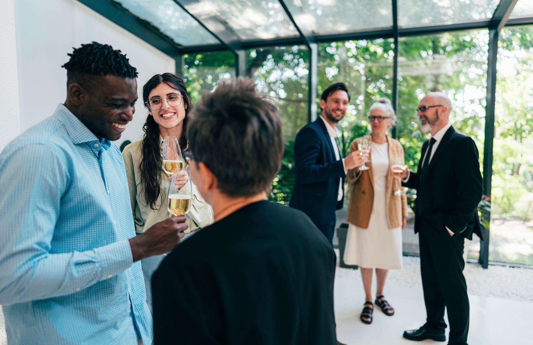 Colleagues enjoying champagne and conversation at a relaxed corporate celebration in a glass-roofed venue.