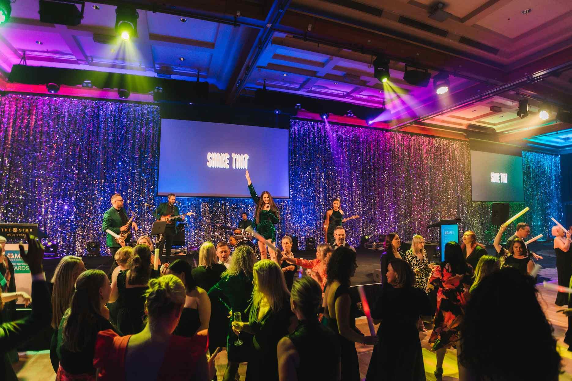 Live band with female lead vocalist performing on stage as guests dance at a corporate awards night.